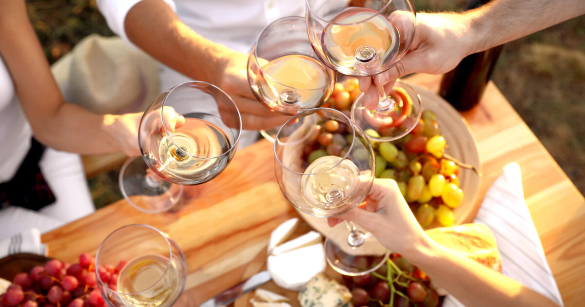 Friends Holding Glasses Of Wine At Table, Closeup